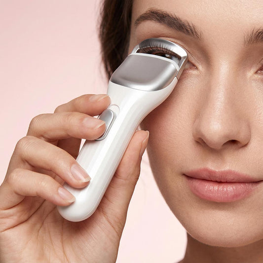Woman using a white skincare device on her eye against a pink background